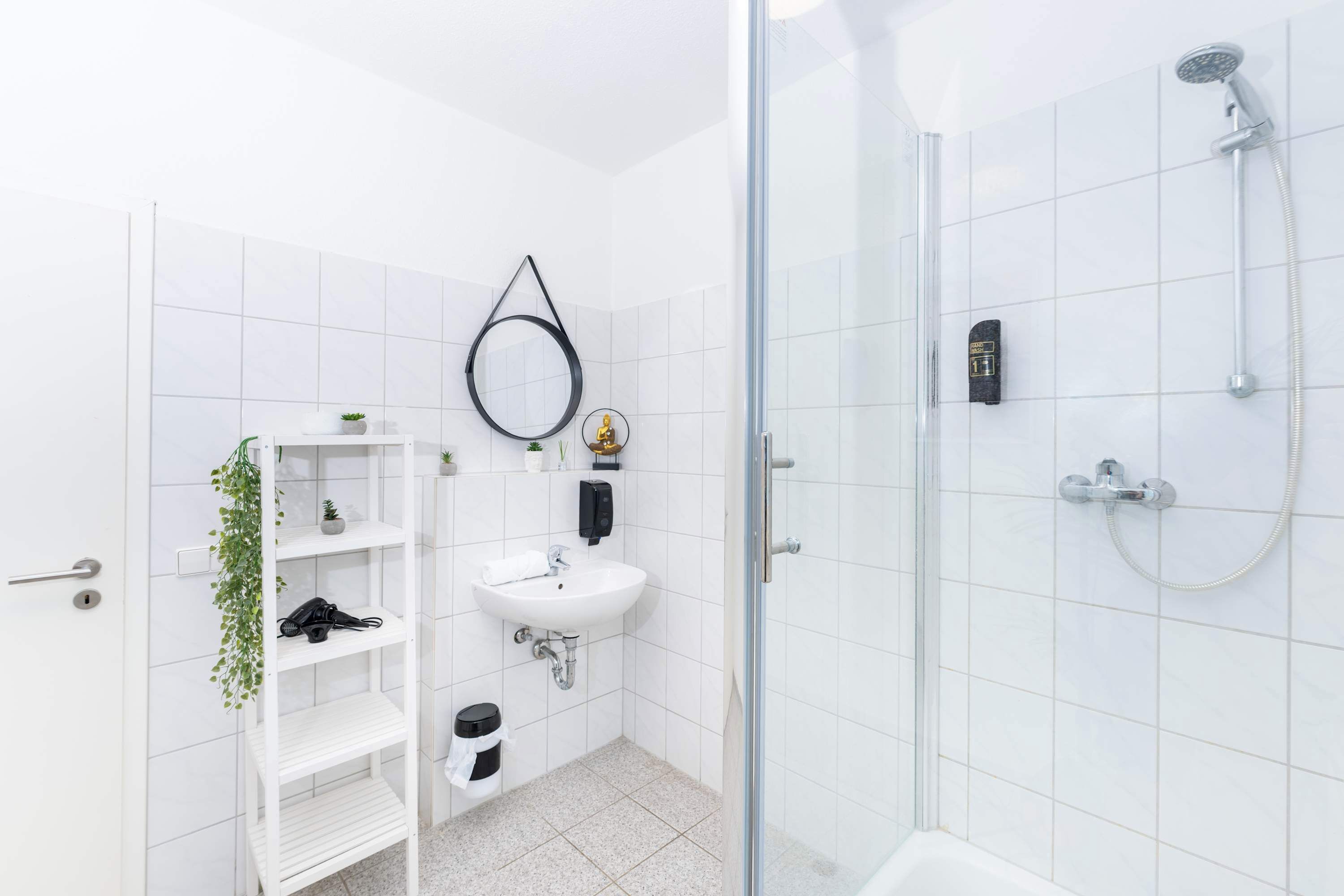 Une salle de bain moderne avec une douche à parois de verre, un lavabo blanc et une étagère contenant des articles de toilette.