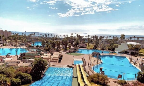A resort with multiple swimming pools, palm trees, and a view of the ocean. - Seaside apartment, air-conditioned (Salou)
