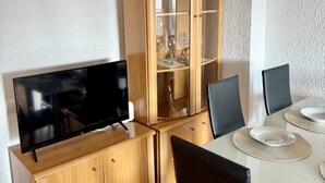 Ruokailutilassa on televisio, joka on sijoitettu puiseen kaappiin, lasikaappi viinilaseille sekä pöytä tuoleineen ja lautuisineen.