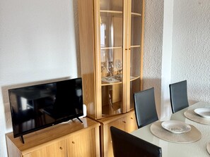A dining area with a TV on a wooden cabinet, a glass cabinet with wine glasses, and a table with chairs and plates. - Seaside apartment, air-conditioned (Salou)