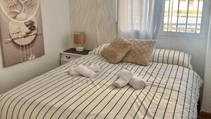 Hotellihuone, jossa on raidallinen sänky, yöpöytä lampun kanssa, seinätaideteos ja ikkuna, josta avautuu näkymä rakennuksiin.