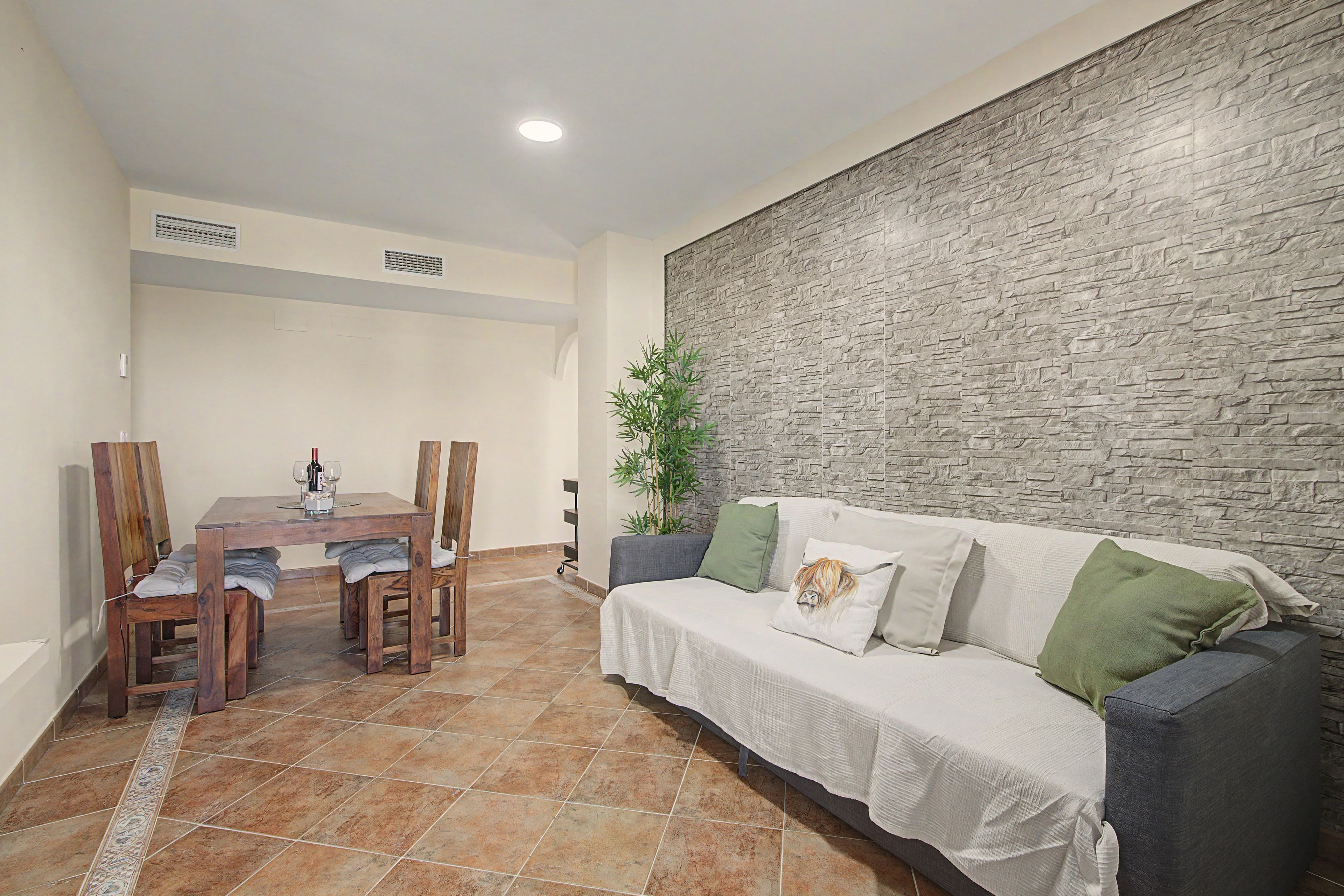 A dining area with a wooden table and chairs, a sofa with cushions, and a textured wall.