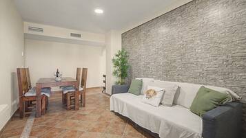 A dining area with a wooden table and chairs, a sofa with cushions, and a textured wall.