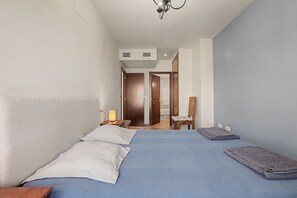 Un dormitorio con cama, almohadas, una mesita de noche con lámpara, una silla y vistas al baño.