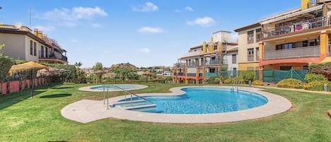 A residential area with two swimming pools, a grassy lawn, and multi-story buildings with balconies.