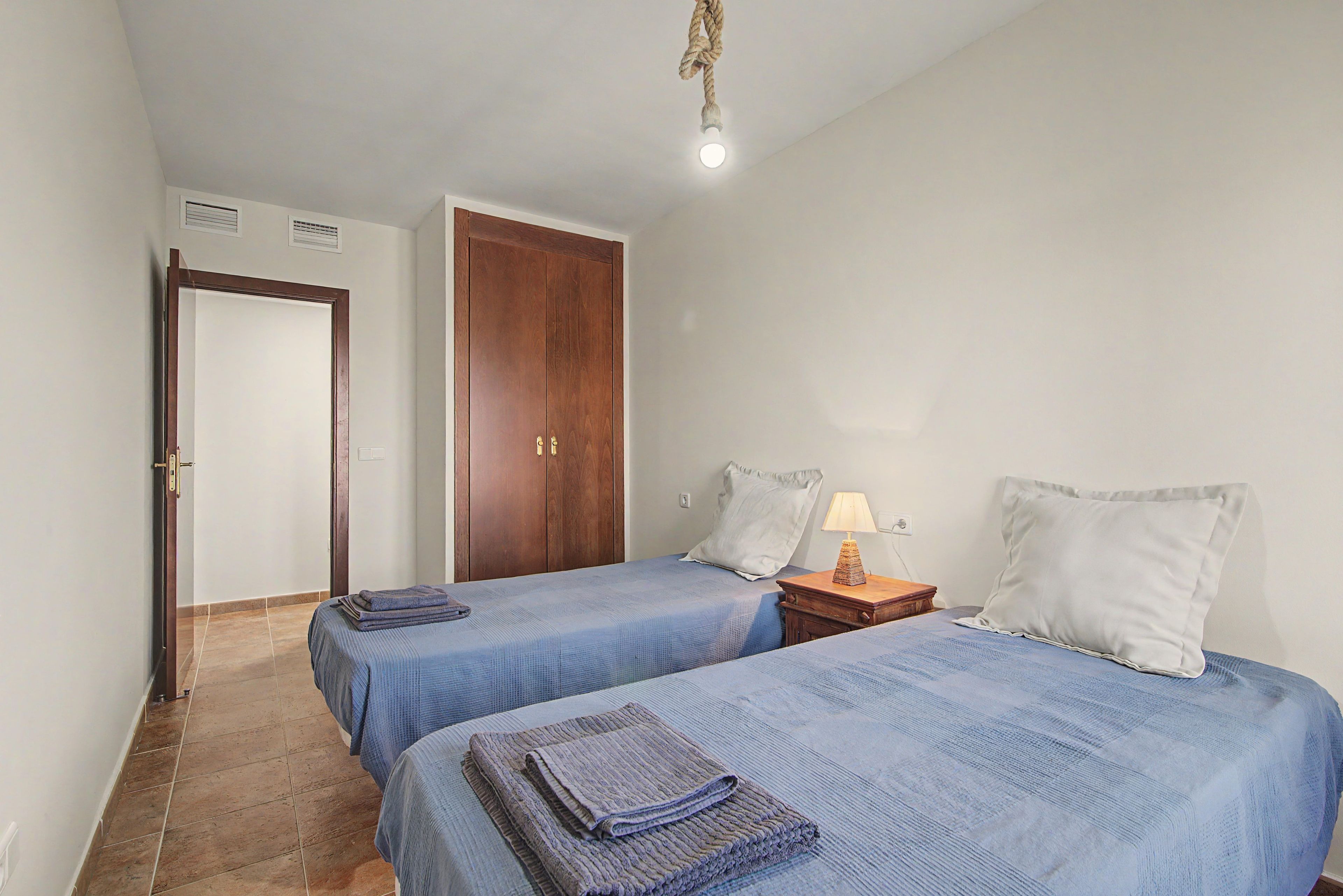 Ein Schlafzimmer mit zwei Einzelbetten, einem Holzschrank, einem Nachttisch mit Lampe und einer Pendelleuchte.