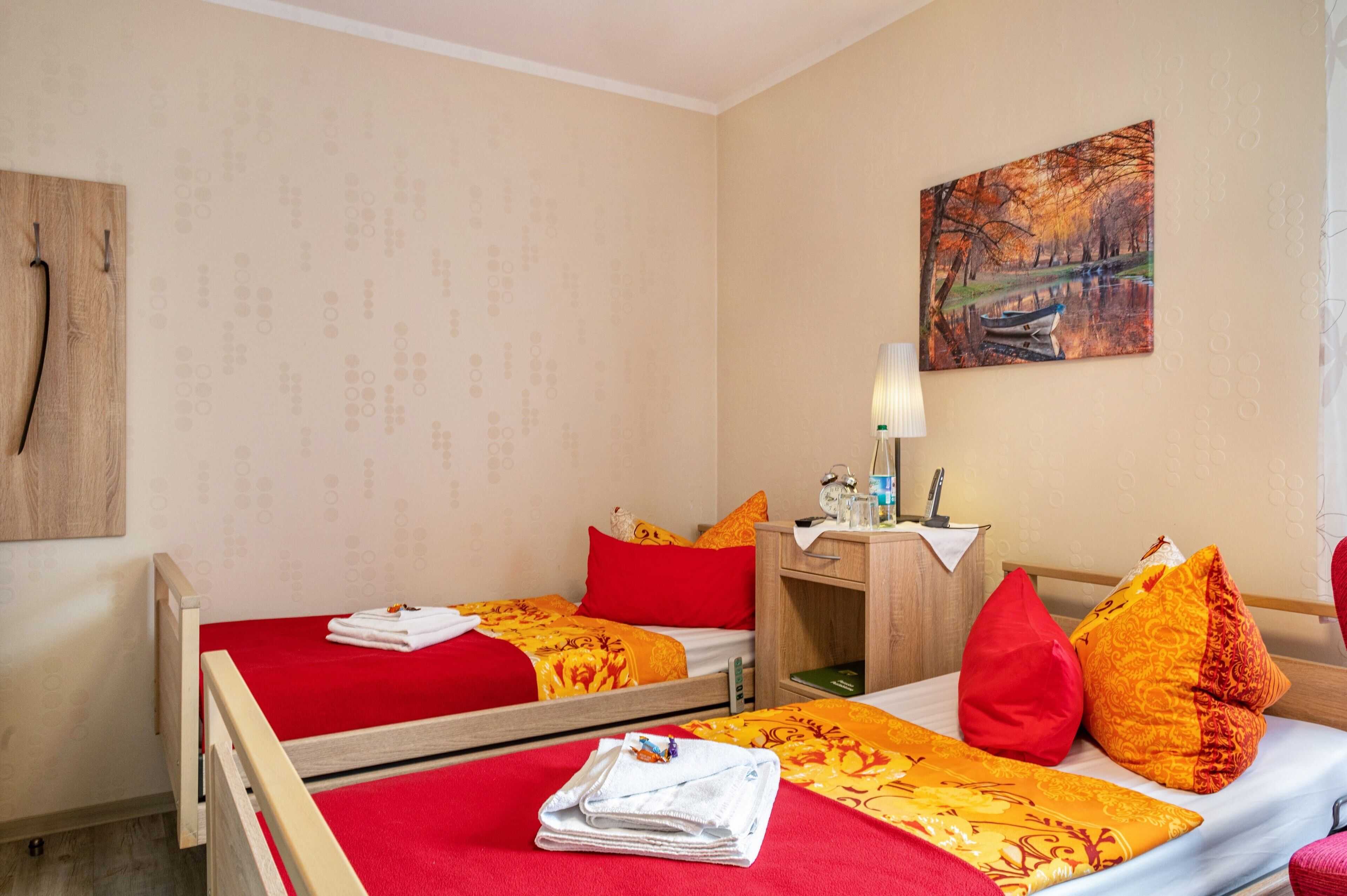 Ein Hotelzimmer mit zwei Einzelbetten, einem Schreibtisch, einem Stuhl, einer Lampe, einem Gemälde und einem Holzkopfteil.