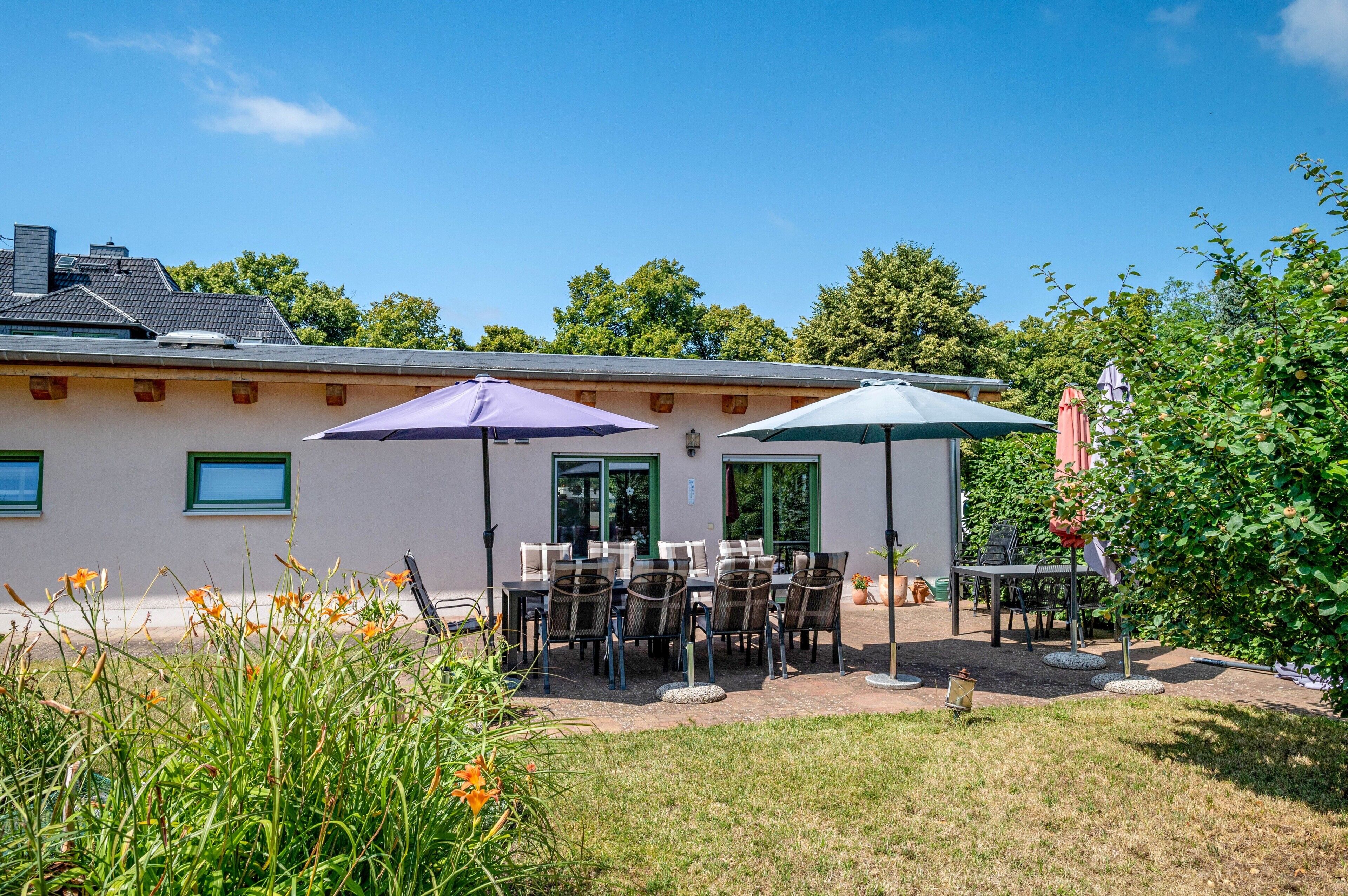 Un espace extérieur aménagé en terrasse, avec des tables et des chaises, deux parasols et un bâtiment en arrière-plan.