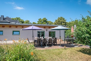 Un espace extérieur aménagé en terrasse, avec des tables et des chaises, deux parasols et un bâtiment en arrière-plan.