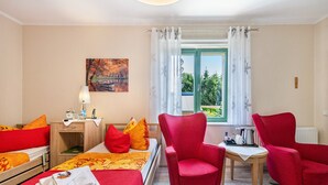 Hotelkamer met een bed, twee rode stoelen, een klein tafeltje met een waterkoker, een schilderij aan de muur en een raam met gordijnen.