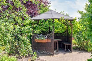 Un kiosque en bois doté d’un toit, entouré d’une végétation luxuriante et de plantes en fleurs.
