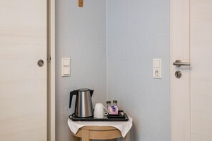Une petite table avec une bouilloire, une cafetière et un plateau contenant des sachets de café.