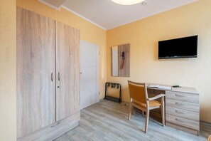 A bedroom with a wardrobe, a desk with a chair, a television, and a radiator.