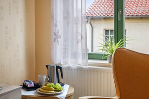 A room with a radiator, a table with a plate of fruit, a coffee pot, and a chair.
