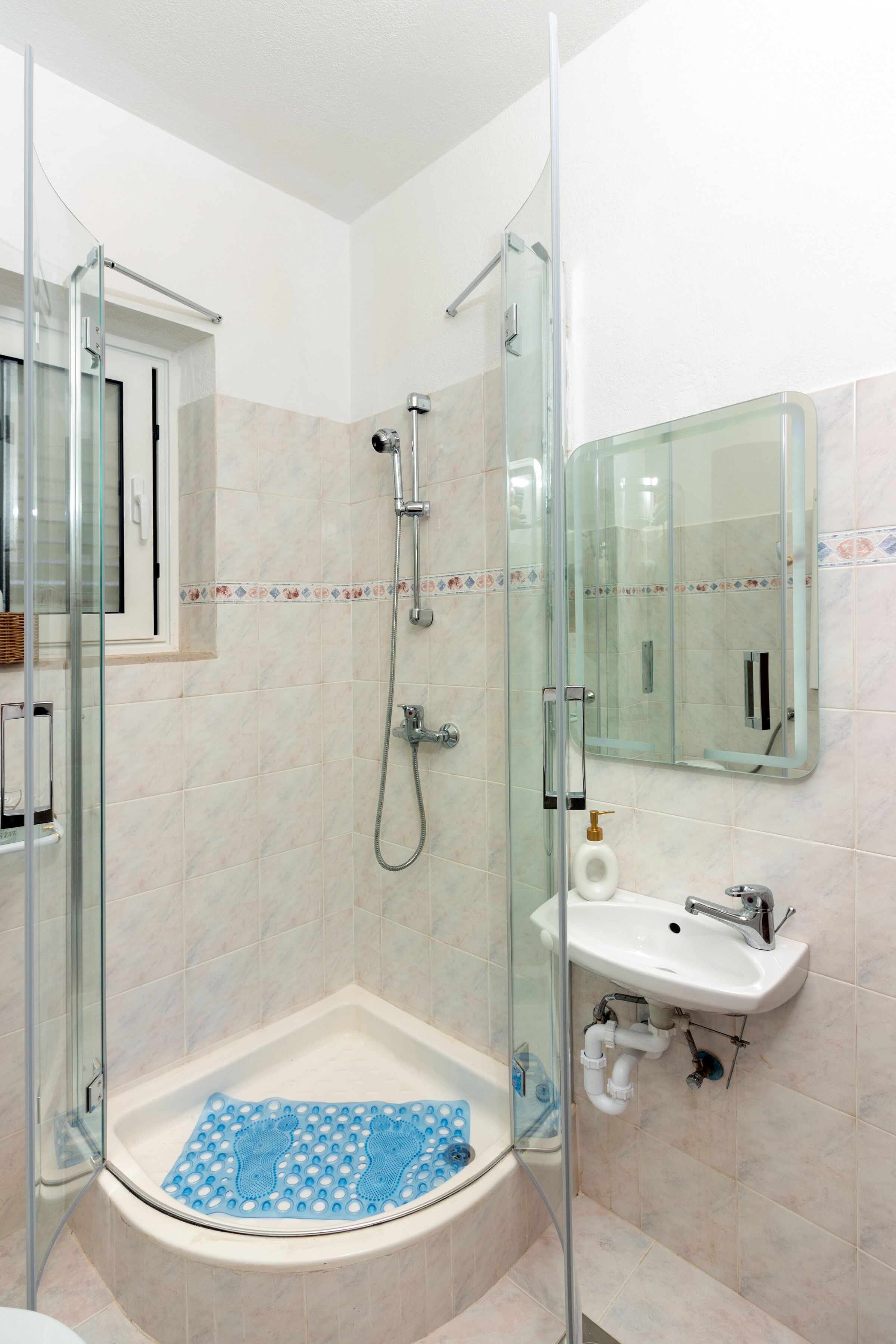 A modern bathroom with a glass-enclosed shower, a white sink, and a mirror.