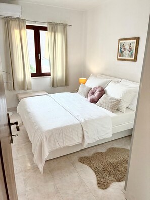 A bedroom with a bed, a window with curtains, a bedside lamp, and a rug. - Beach Nest (Split)
