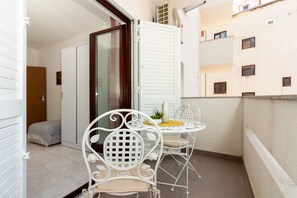 A balcony with a white metal table and chairs, a potted plant, and a view of a building with windows. - Beach Nest (Split)
