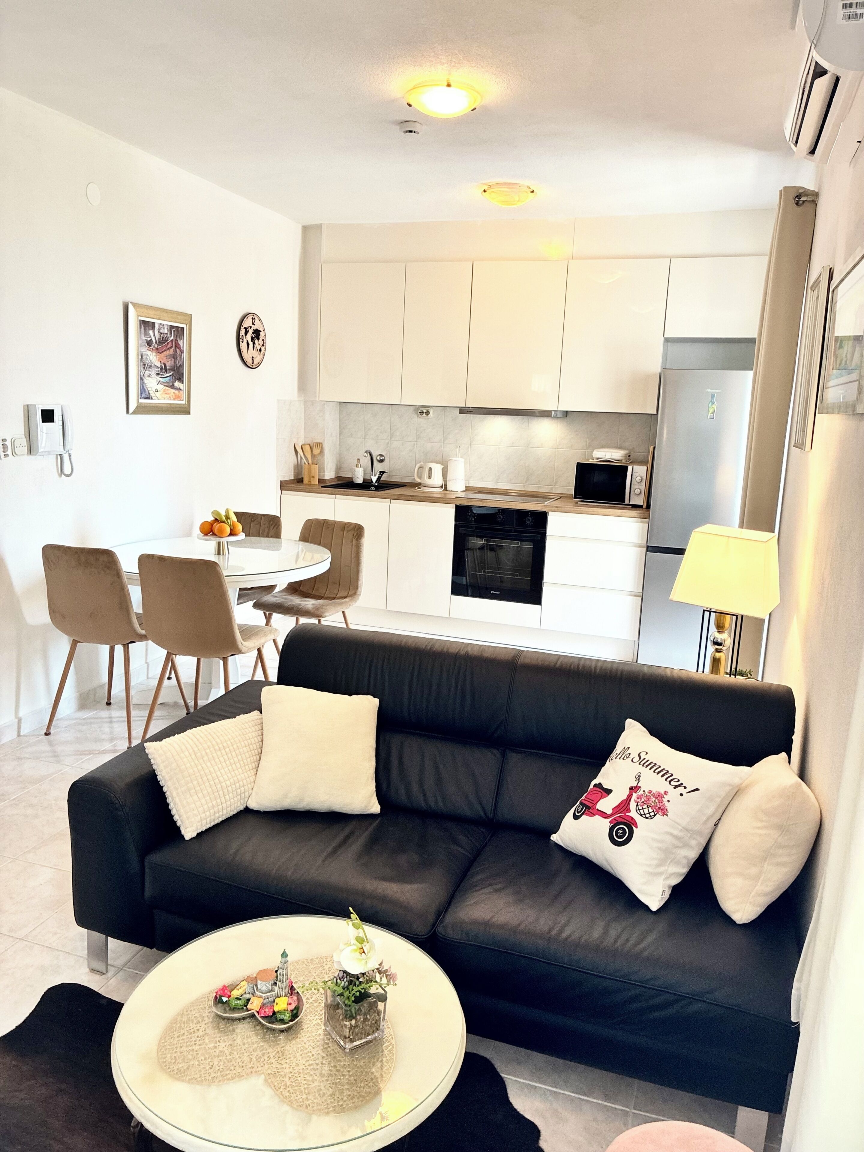 Una sala moderna con un sofá de cuero negro, una mesa de centro de vidrio y un comedor con mesa y sillas blancas.