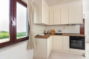 A kitchen with white cabinets, a wooden countertop, a black stove, and a window with curtains. - Beach Nest (Split)