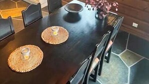 Een eetruimte met een donker houten tafel, zwarte stoelen en geweven plaatszetters.