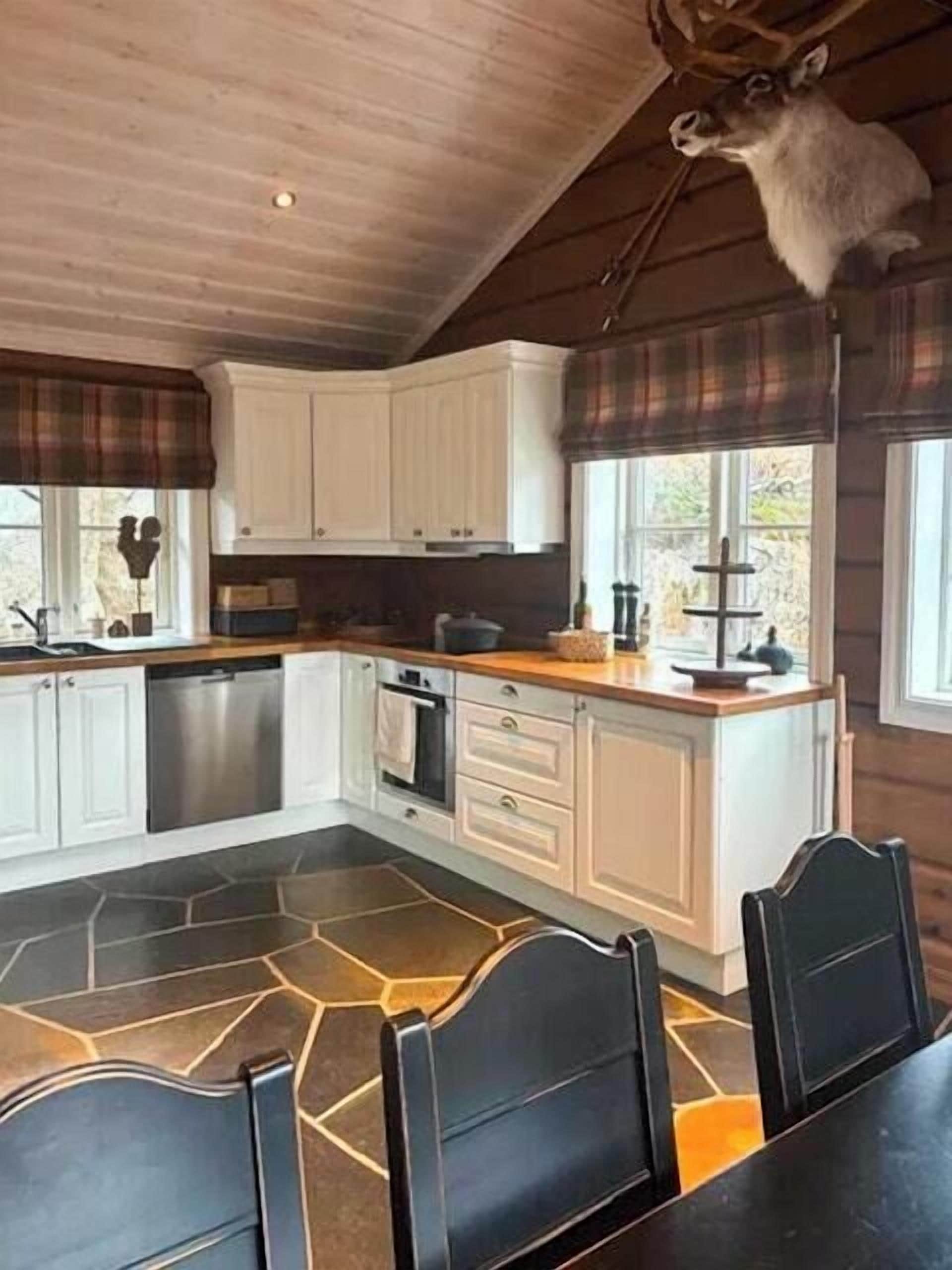 A kitchen with white cabinets, a stone floor, and a dining area with black chairs.