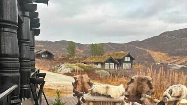 Een houten terras met rustieke meubels en uitzicht op een huis in een glooiend landschap.