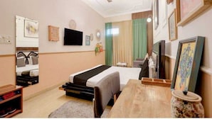 Habitación de hotel con cama, escritorio, silla, ventilador de techo y cuadros en las paredes.