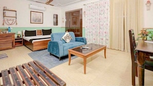 Una habitación con una cama, un sofá azul, una mesa de centro de madera, un banco de madera y una mesa de comedor con sillas.