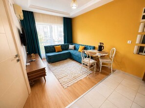 A modern living room with a sectional sofa, a coffee table, and a dining area. - Kampüs Apart Otel (ANTALYA)