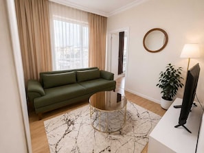 A living room with a green sofa, a glass coffee table, a round mirror, a lamp, and a potted plant. - Kampüs Apart Otel (ANTALYA)