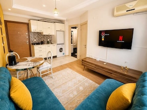 A modern living room with a sofa, a coffee table, and a television mounted on the wall. - Kampüs Apart Otel (ANTALYA)