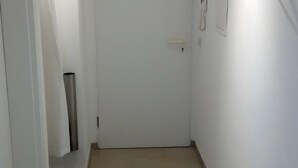 Een smalle gang met een witte deur, een lichtschakelaar en een telefoon aan de muur.