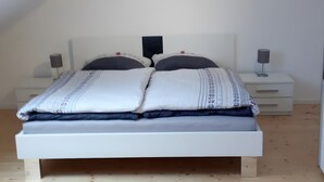 Een bed met een wit hoofdeinde, twee nachtkastjes en een nachtkastje met een lamp.