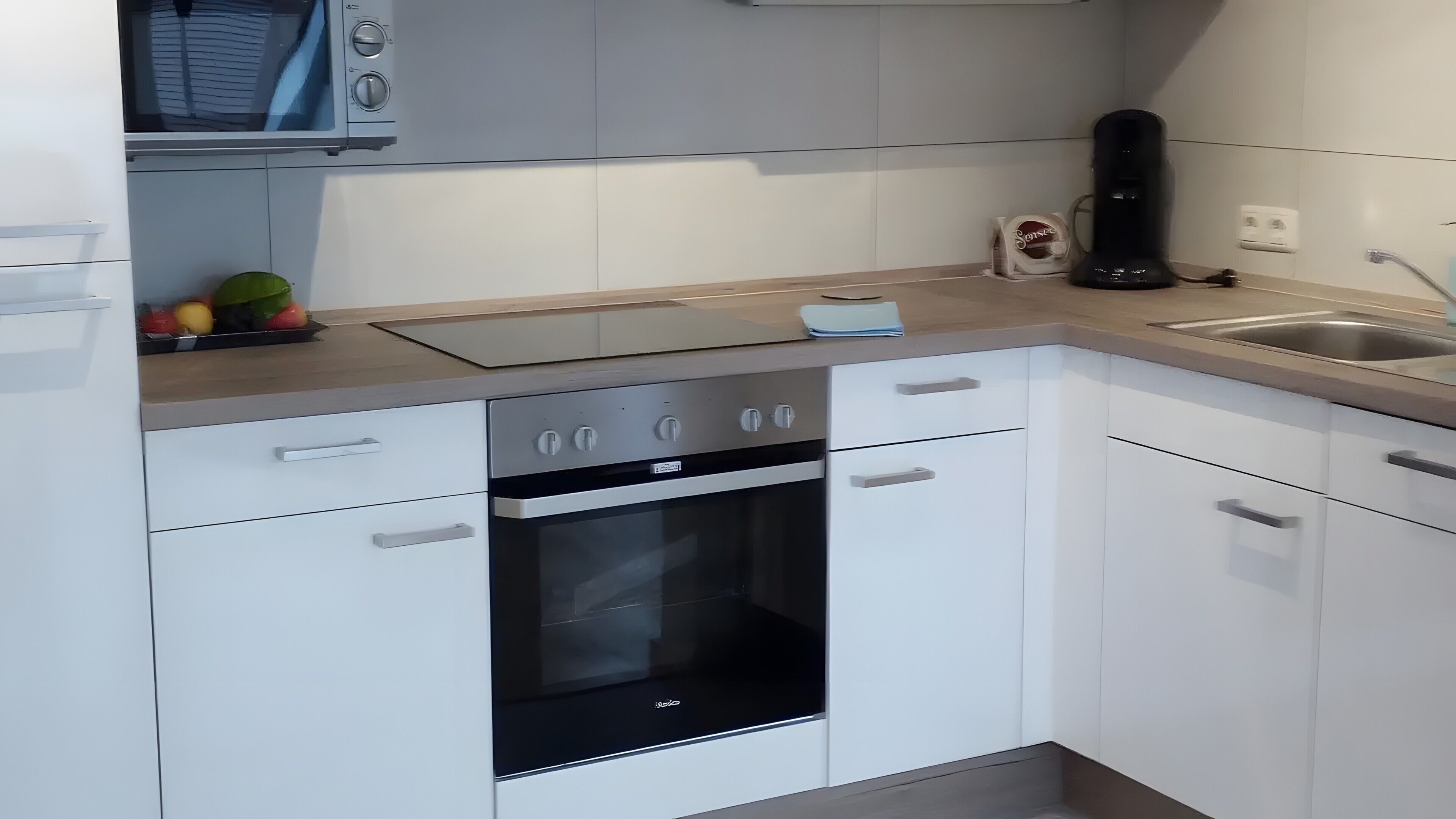 Una cucina moderna con mobili bianchi, forno a incasso e lavello in acciaio inossidabile.