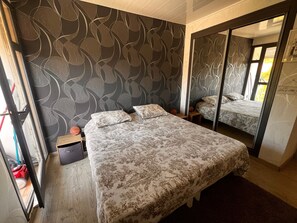 A bedroom with a bed, a nightstand, a mirror, and a wardrobe. - 3-room apartment near the beach - 57m² (Argelès-sur-Mer)