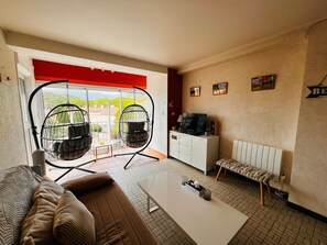 A living room with a sofa, a coffee table, a TV, and two hanging chairs. - 3-room apartment near the beach - 57m² (Argelès-sur-Mer)