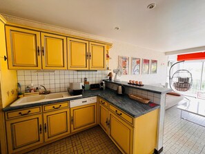 A kitchen with yellow cabinets, a sink, a microwave, and a hanging chair. - 3-room apartment near the beach - 57m² (Argelès-sur-Mer)
