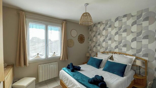 Ein Schlafzimmer mit Bett, Nachttischen, einem Fenster mit Vorhängen, einem Heizkörper und einer Wand mit geometrischem Muster.