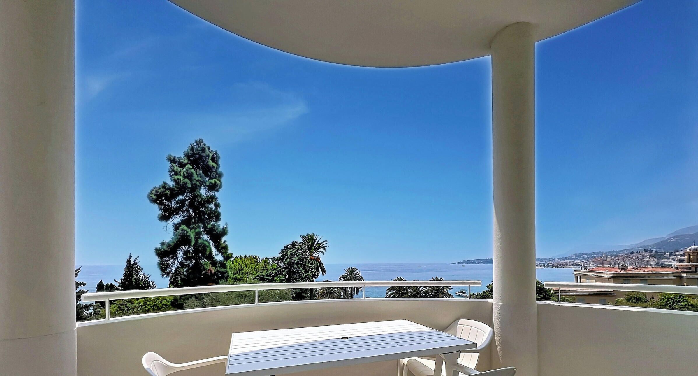 A balcony with a table and chairs, overlooking a coastal cityscape.