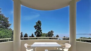 Un balcon avec une table et des chaises, offrant une vue sur la côte, avec des arbres et la mer.