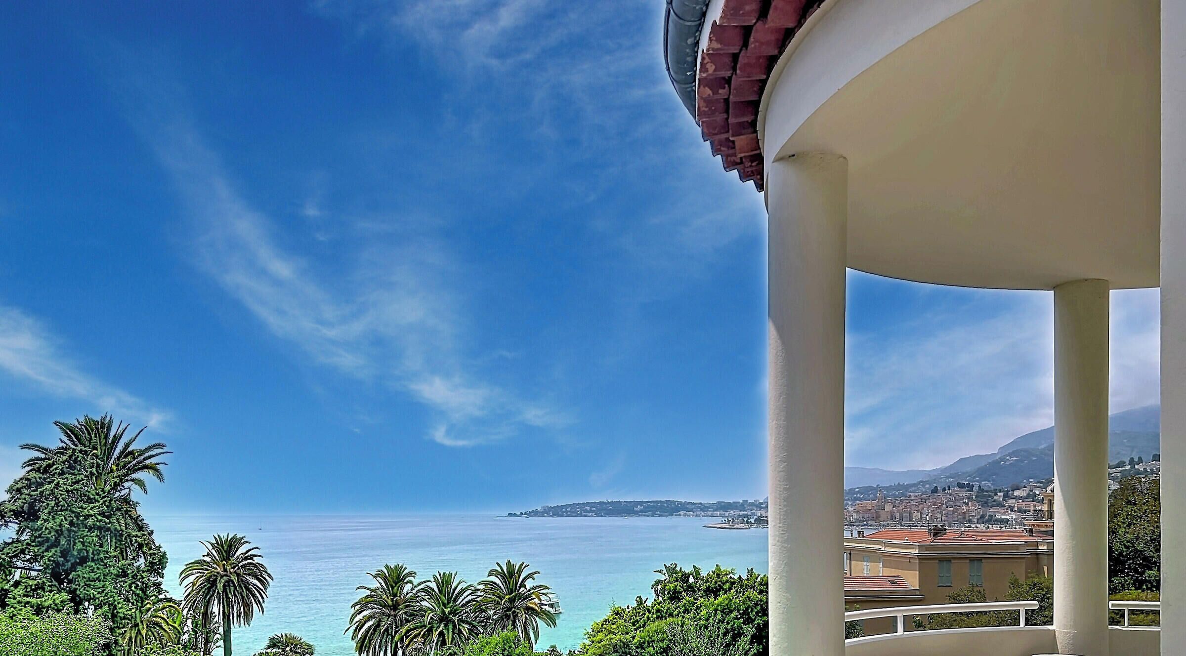 A balcony with a clear view of the sea and distant cityscape.