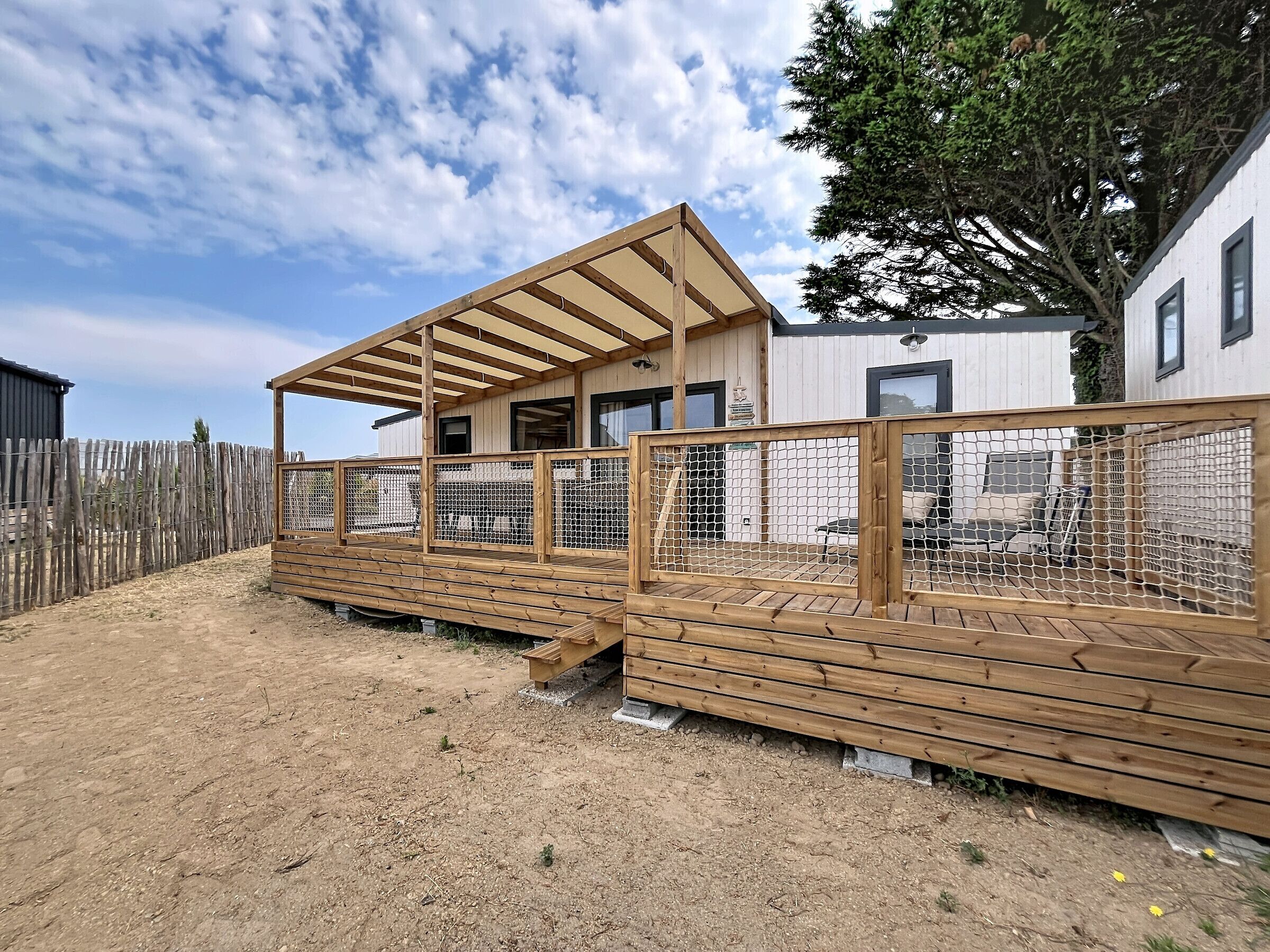 Una terraza de madera con un espacio de estar techado, un cerramiento y un edificio con ventanas.