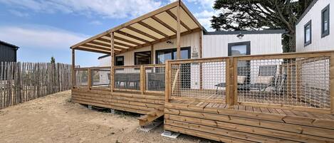Una terraza de madera con un espacio de estar techado, un cerramiento y un edificio con ventanas.