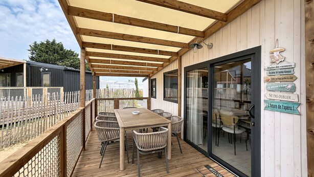 Eine Holzterrasse mit Tisch und Stühlen, ein Glastür-Eingang und ein Schild mit französischem Text.