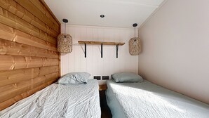 Ein Zimmer mit zwei Einzelbetten, Holzwandverkleidung an einer Wand und einem Regal mit hängenden Körben.