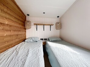 A room with two single beds, wooden paneling on one wall, and a shelf with hanging baskets. - House with parking - 6 guests (Saint-Pair-sur-Mer)