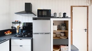 Eine Küche mit Herd, Mikrowelle und Kühlschrank. Es gibt Schränke und ein Regal mit Küchenutensilien.