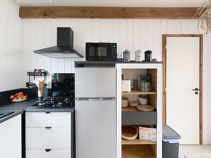 A kitchen with a stove, microwave, and refrigerator. There are cabinets and a shelf with kitchenware. - House with parking - 6 guests (Saint-Pair-sur-Mer)