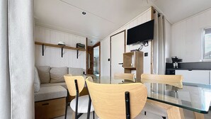 Ein modernes Interieur mit einem Essbereich, der einen Glastisch und Holzstühle, eine Couch und einen an der Wand befestigten Fernseher umfasst.