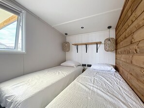 Een kleine, compacte kamer met twee eenpersoonsbedden, een houten wandpaneel, een raam en een plafondlamp.
